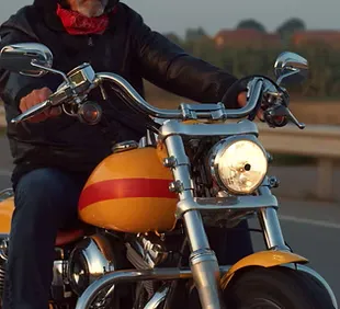 Rider in black leather and red scarf enjoying an evening motorcycle ride on a custom orange bike – secure your passion for the road with expert motorcycle insurance from a professional insurance agent.